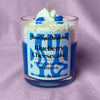 Photo of dessert-style candle with blueberries labeled blueberry cheesecake on a light pink background.