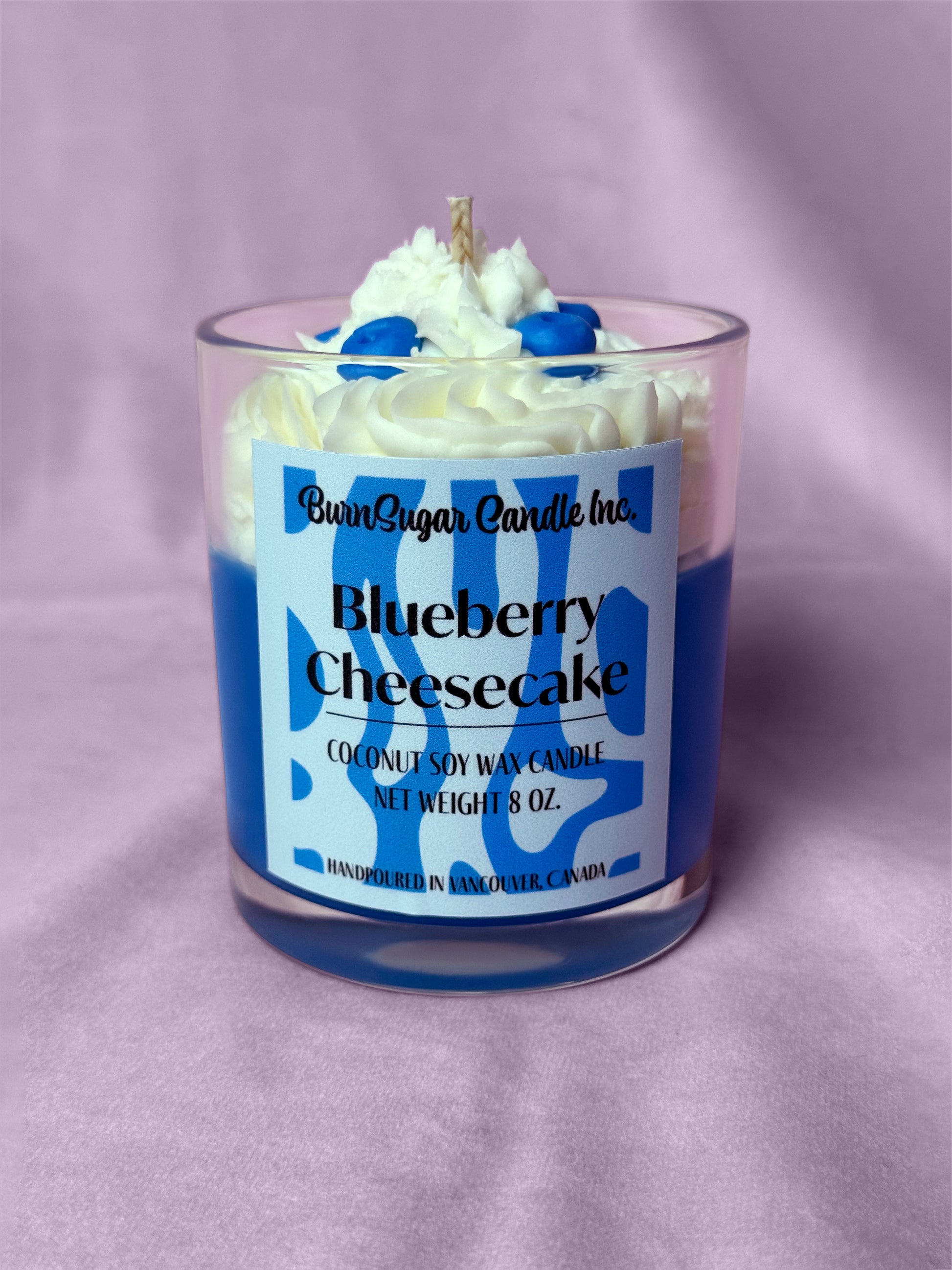 Photo of dessert-style candle with blueberries labeled blueberry cheesecake on a light pink background.