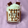 Candle with whipped cream and chocolate pieces on a purple background