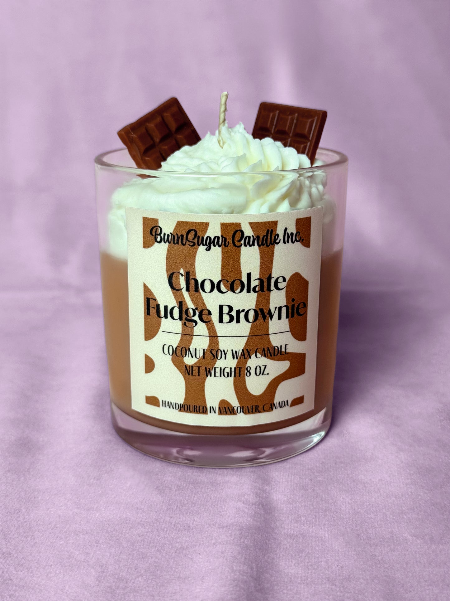 Candle with whipped cream and chocolate pieces on a purple background