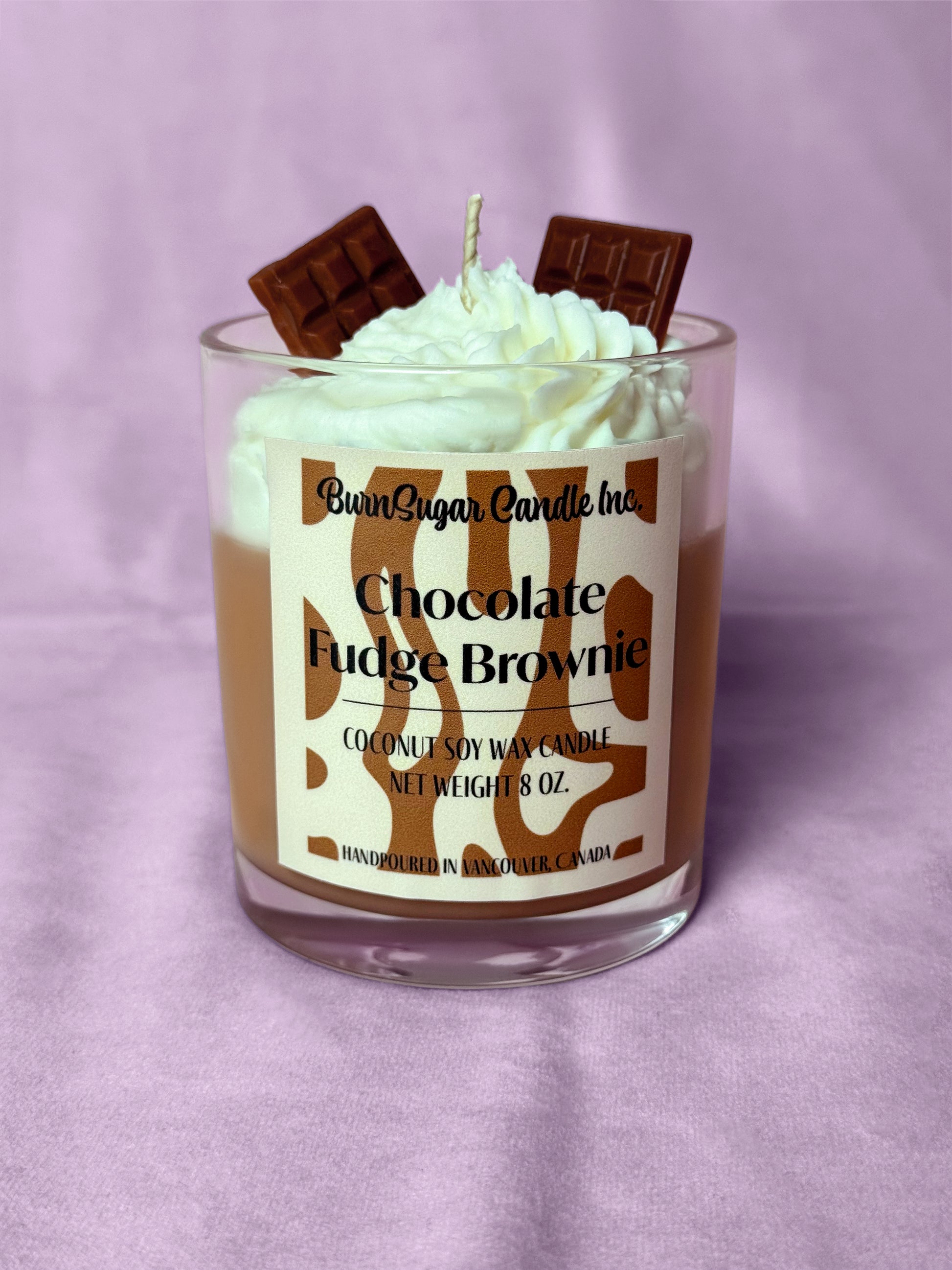 Candle with whipped cream and chocolate pieces on a purple background