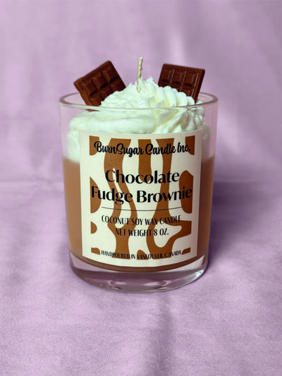 Candle with whipped cream and chocolate pieces on a purple background