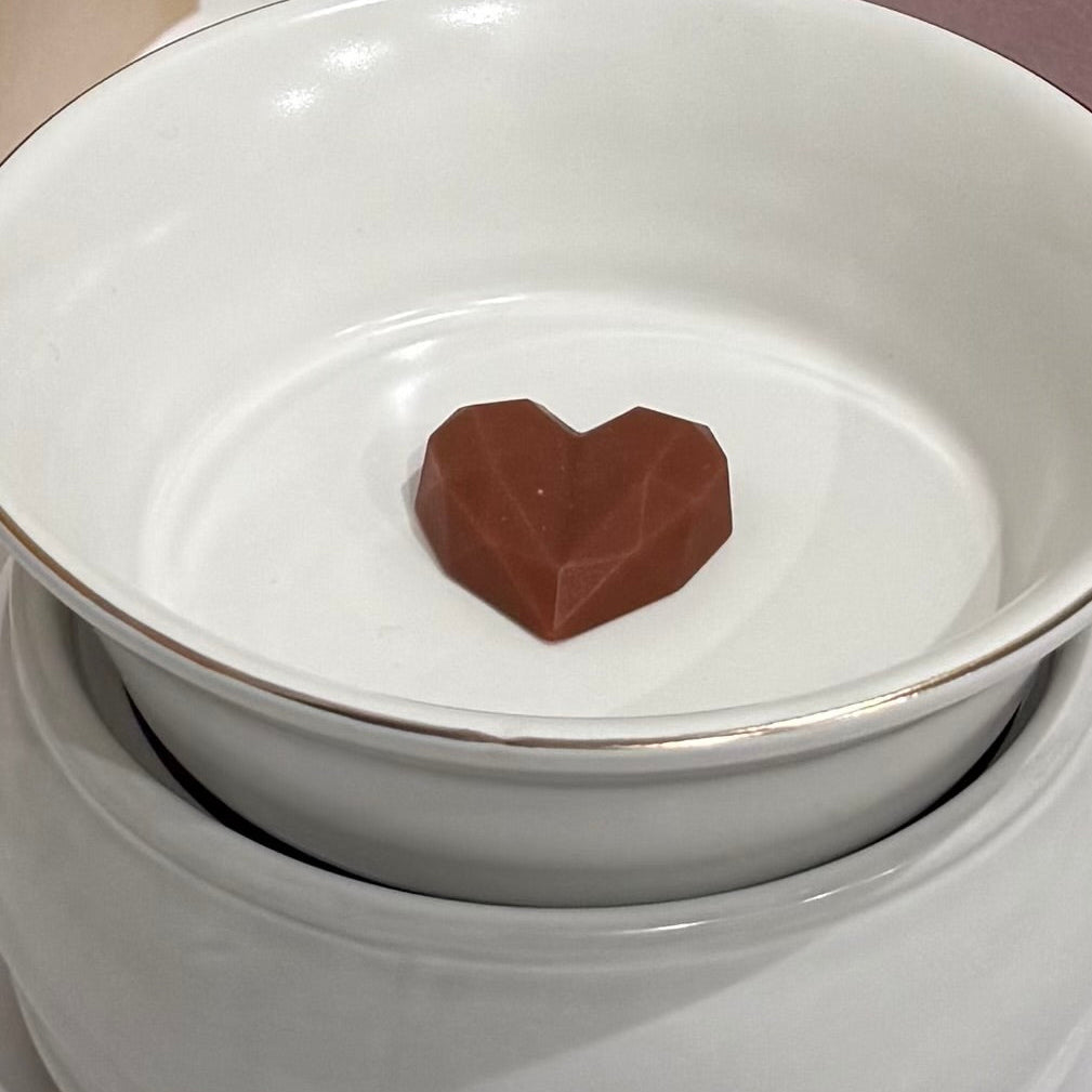 Heart-shaped chocolate wax melt in a white melting bowl on a light background